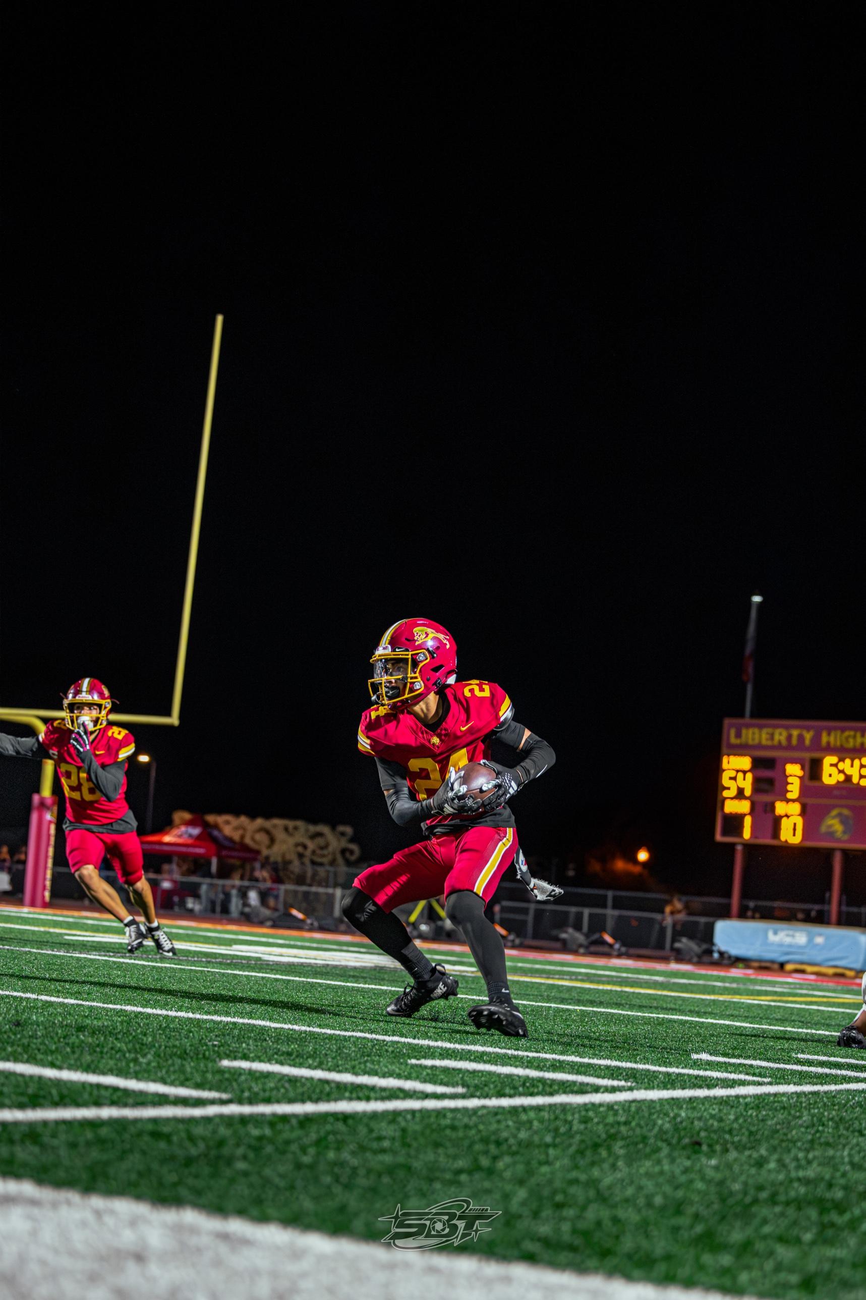 Liberty's #24 running with the ball, Liberty High School scoreboard visible in the background