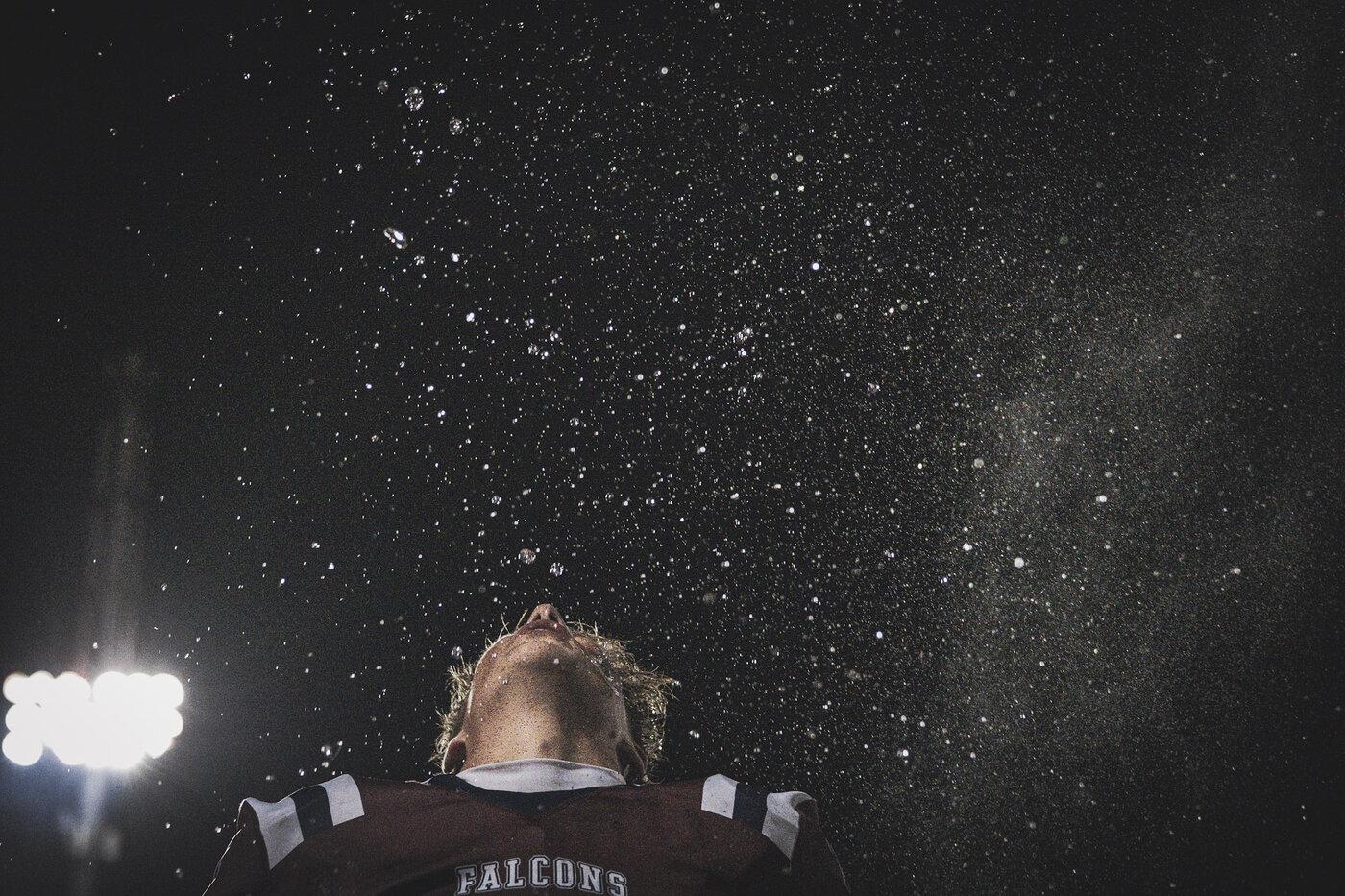 Freedom Falcons player looking up into stadium lights and rain